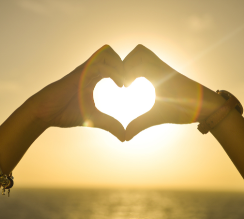 Des doigts joints formant un coeur dans le soleil couchant